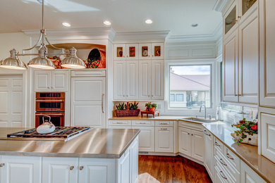 Example of a mid-sized transitional l-shaped light wood floor eat-in kitchen design in Denver with an undermount sink, raised-panel cabinets, white cabinets, stainless steel countertops, white backsplash, stainless steel appliances and two islands