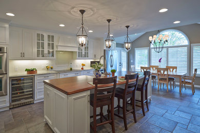 Eat-in kitchen - large transitional single-wall travertine floor eat-in kitchen idea in Baltimore with a farmhouse sink, beaded inset cabinets, white cabinets, granite countertops, white backsplash, ceramic backsplash, stainless steel appliances and an island
