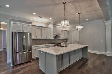 Inspiration for a large transitional single-wall brown floor and dark wood floor open concept kitchen remodel in Atlanta with an undermount sink, stainless steel appliances, raised-panel cabinets, white cabinets, marble countertops, gray backsplash, glass tile backsplash and an island