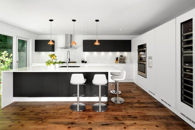 Inspiration for a contemporary medium tone wood floor and brown floor kitchen remodel in Toronto with an undermount sink, flat-panel cabinets, white backsplash, glass sheet backsplash, stainless steel appliances and an island