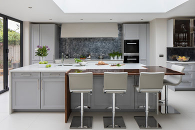ロンドンにある高級な広いトランジショナルスタイルのおしゃれなキッチン (ドロップインシンク、落し込みパネル扉のキャビネット、グレーのキャビネット、人工大理石カウンター、メタリックのキッチンパネル、ミラータイルのキッチンパネル、黒い調理設備、セラミックタイルの床、白い床) の写真