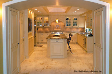 Large elegant u-shaped marble floor and beige floor enclosed kitchen photo in Miami with an undermount sink, raised-panel cabinets, white cabinets, granite countertops, beige backsplash, ceramic backsplash, stainless steel appliances and an island