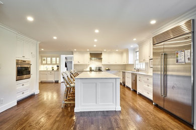 Example of a large light wood floor and brown floor kitchen design in New York with an undermount sink, recessed-panel cabinets, white cabinets, marble countertops, white backsplash, subway tile backsplash, stainless steel appliances, an island and gray countertops