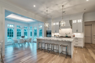 Example of a mid-sized classic u-shaped light wood floor and beige floor eat-in kitchen design in New York with an undermount sink, flat-panel cabinets, white cabinets, marble countertops, white backsplash, ceramic backsplash, stainless steel appliances, an island and white countertops