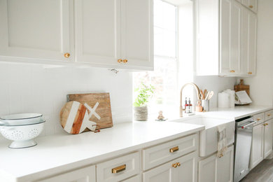 Eat-in kitchen - large traditional single-wall eat-in kitchen idea in Dallas with shaker cabinets, white cabinets, solid surface countertops, stainless steel appliances, an island, white countertops, a farmhouse sink, white backsplash and porcelain backsplash