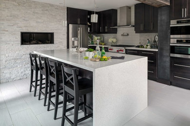Photo of a large traditional l-shaped open plan kitchen in Toronto with a submerged sink, shaker cabinets, black cabinets, grey splashback, metro tiled splashback, stainless steel appliances, porcelain flooring, an island and grey floors.