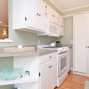 Design ideas for a small beach style galley eat-in kitchen in Seattle with beaded inset cabinets, white cabinets, laminate benchtops, white appliances and light hardwood floors.