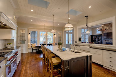 Photo of a large rural l-shaped kitchen/diner in San Francisco with a belfast sink, recessed-panel cabinets, white cabinets, stainless steel appliances, medium hardwood flooring and an island.
