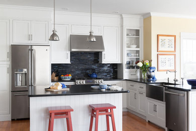 Mid-sized beach style u-shaped medium tone wood floor and brown floor open concept kitchen photo in Boston with a farmhouse sink, shaker cabinets, white cabinets, solid surface countertops, blue backsplash, matchstick tile backsplash, stainless steel appliances and an island