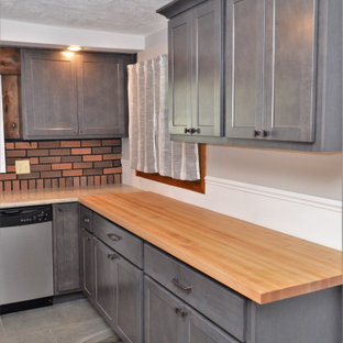 Mittelgroße Landhausstil Wohnküche ohne Insel in U-Form mit Unterbauwaschbecken, Schrankfronten im Shaker-Stil, grauen Schränken, Arbeitsplatte aus Holz, Küchenrückwand in Rot, Rückwand aus Backstein, Küchengeräten aus Edelstahl, Schieferboden, grauem Boden und brauner Arbeitsplatte in Sonstige