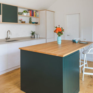Offene, Mittelgroße Moderne Küche in L-Form mit Einbauwaschbecken, flächenbündigen Schrankfronten, Küchengeräten aus Edelstahl, Kücheninsel, beiger Arbeitsplatte, orangefarbenen Schränken, Arbeitsplatte aus Holz, hellem Holzboden und beigem Boden in Oxfordshire