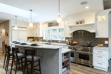 Example of a large transitional l-shaped light wood floor and brown floor eat-in kitchen design in Philadelphia with a farmhouse sink, recessed-panel cabinets, white cabinets, marble countertops, gray backsplash, subway tile backsplash, stainless steel appliances, an island and gray countertops