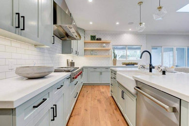 Trendy medium tone wood floor eat-in kitchen photo in San Diego with a farmhouse sink, recessed-panel cabinets, green cabinets, granite countertops, white backsplash, subway tile backsplash, stainless steel appliances, an island and white countertops