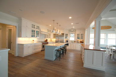 Exempel på ett stort klassiskt kök, med en rustik diskho, luckor med infälld panel, vita skåp, bänkskiva i kvarts, vitt stänkskydd, stänkskydd i tunnelbanekakel, rostfria vitvaror, ljust trägolv och flera köksöar