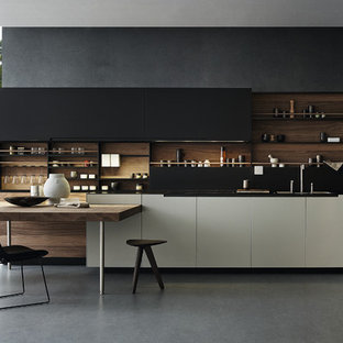 Imagen de cocina en L, actual, con puertas de armario negras, electrodomésticos negros, armarios con paneles lisos, salpicadero negro, suelo de cemento y encimeras negras