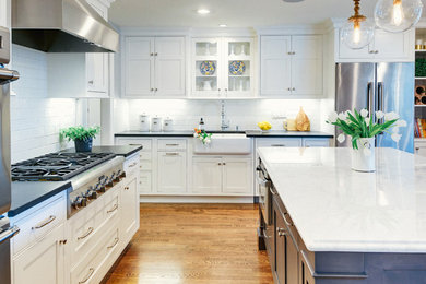 Transitional l-shaped medium tone wood floor kitchen photo in Philadelphia with a farmhouse sink, recessed-panel cabinets, white cabinets, white backsplash, subway tile backsplash, stainless steel appliances and an island