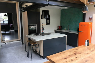 Photo of a medium sized contemporary kitchen/diner in London with a single-bowl sink, flat-panel cabinets, black cabinets, concrete worktops, green splashback, ceramic splashback, black appliances, concrete flooring, an island and grey floors.