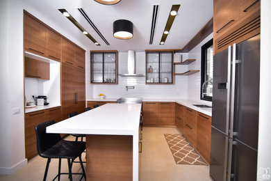 Example of a mid-sized trendy u-shaped porcelain tile and beige floor kitchen design in Los Angeles with quartz countertops, white backsplash, subway tile backsplash, an undermount sink, flat-panel cabinets, medium tone wood cabinets, stainless steel appliances, an island and white countertops