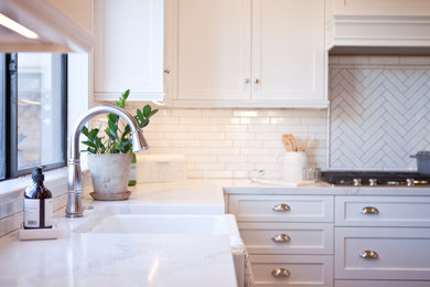 Example of a mid-sized beach style u-shaped medium tone wood floor eat-in kitchen design in San Diego with a farmhouse sink, shaker cabinets, white cabinets, quartz countertops, white backsplash, ceramic backsplash, stainless steel appliances and an island