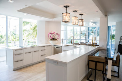 Inspiration for a contemporary u-shaped vinyl floor eat-in kitchen remodel in Miami with an undermount sink, shaker cabinets, white cabinets, solid surface countertops, white backsplash, stainless steel appliances and a peninsula