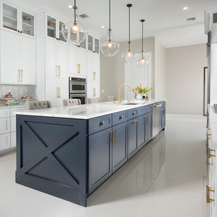 Design ideas for a transitional galley kitchen in Miami with an undermount sink, shaker cabinets, white cabinets, white splashback, marble splashback, stainless steel appliances, with island and white floor.