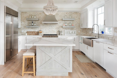 Eat-in kitchen - mid-sized coastal l-shaped light wood floor and brown floor eat-in kitchen idea in New York with a farmhouse sink, white cabinets, quartz countertops, beige backsplash, ceramic backsplash, stainless steel appliances and an island