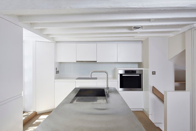 Photo of a medium sized contemporary kitchen in London with a single-bowl sink, flat-panel cabinets, white cabinets, stainless steel worktops, white splashback, stainless steel appliances and an island.