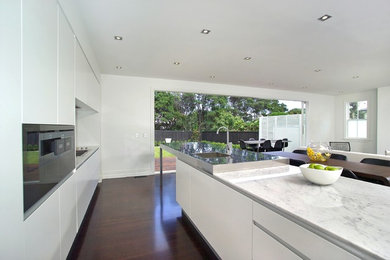 Design ideas for an expansive contemporary l-shaped open plan kitchen in Auckland with flat-panel cabinets, white cabinets, an island, a single-bowl sink, marble worktops, white splashback, glass sheet splashback, stainless steel appliances and dark hardwood flooring.