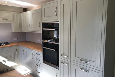 Design ideas for a large traditional u-shaped kitchen/diner in Surrey with a built-in sink, shaker cabinets, green cabinets, wood worktops, stainless steel appliances, laminate floors, grey floors and brown worktops.