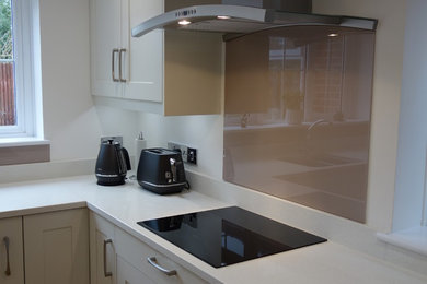Photo of a medium sized contemporary l-shaped kitchen/diner in Dorset with an integrated sink, shaker cabinets, white cabinets, quartz worktops, brown splashback, glass sheet splashback, black appliances, vinyl flooring and no island.