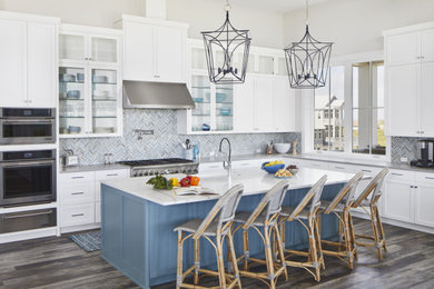 Example of a huge beach style l-shaped vinyl floor and brown floor open concept kitchen design in Other with an undermount sink, shaker cabinets, white cabinets, quartz countertops, stainless steel appliances, an island, gray backsplash, mosaic tile backsplash and gray countertops