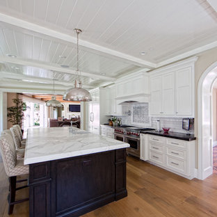 Mid-sized traditional enclosed kitchen remodeling - Example of a mid-sized classic single-wall medium tone wood floor and brown floor enclosed kitchen design in Orange County with a farmhouse sink, shaker cabinets, white cabinets, marble countertops, white backsplash, subway tile backsplash, stainless steel appliances and an island