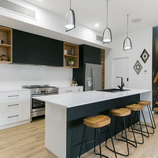 Photo of a contemporary galley kitchen in Adelaide with a drop-in sink, flat-panel cabinets, white cabinets, white splashback, stainless steel appliances, light hardwood floors, with island, beige floor and white benchtop.