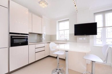 Inspiration for a modern kitchen in London with flat-panel cabinets, white cabinets, beige splashback, glass sheet splashback and black appliances.