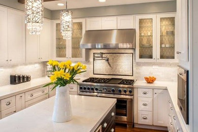 Inspiration for a mid-sized transitional u-shaped medium tone wood floor enclosed kitchen remodel in San Francisco with recessed-panel cabinets, white cabinets, quartz countertops, white backsplash, stone tile backsplash, stainless steel appliances and an island