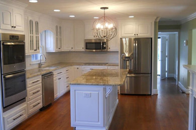 Mid-sized elegant l-shaped medium tone wood floor and brown floor kitchen photo in Other with an undermount sink, raised-panel cabinets, white cabinets, granite countertops, white backsplash, subway tile backsplash, stainless steel appliances and an island