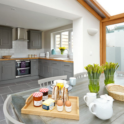 Example of a beach style gray floor eat-in kitchen design in London with a drop-in sink, shaker cabinets, gray cabinets, wood countertops, white backsplash, subway tile backsplash, stainless steel appliances and no island