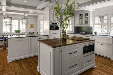 Example of a classic dark wood floor kitchen design in Portland with a farmhouse sink, recessed-panel cabinets, white cabinets, gray backsplash, subway tile backsplash and an island