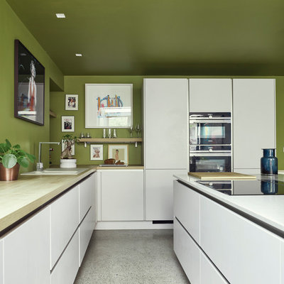 Inspiration for a mid-sized contemporary l-shaped white floor and terrazzo floor kitchen remodel in Dublin with white cabinets, wood countertops, an island, a drop-in sink, flat-panel cabinets, green backsplash and black appliances