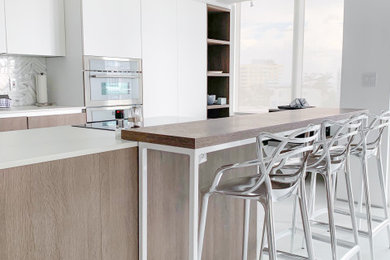 Foto de cocina comedor actual de tamaño medio con puertas de armario blancas, electrodomésticos de acero inoxidable, una isla y encimeras blancas