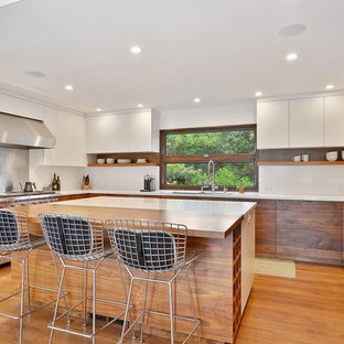 Idee per una cucina a L minimalista con ante lisce, top in quarzo composito, paraspruzzi bianco, paraspruzzi in lastra di pietra, elettrodomestici in acciaio inossidabile, pavimento in legno massello medio, isola, pavimento marrone e ante in legno bruno