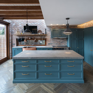 Modelo de cocina comedor industrial, de tamaño medio, con fregadero sobremueble, armarios estilo shaker, puertas de armario azules, encimera de cuarzo compacto, electrodomésticos negros, suelo de madera oscura, una isla y encimeras grises