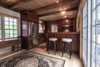 Inspiration for a small farmhouse l-shaped light wood floor enclosed kitchen remodel in Portland Maine with a farmhouse sink, stainless steel appliances, a peninsula, recessed-panel cabinets, dark wood cabinets and red backsplash