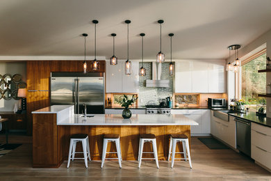 Example of a mid-sized trendy l-shaped light wood floor and beige floor open concept kitchen design in Other with a farmhouse sink, flat-panel cabinets, white cabinets, granite countertops, white backsplash, glass tile backsplash, stainless steel appliances and an island