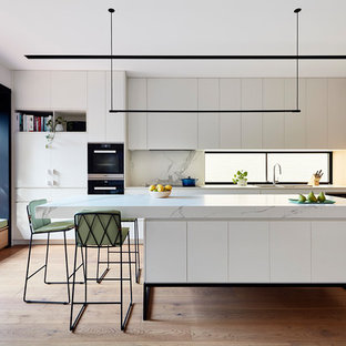 Design ideas for a contemporary galley kitchen in Melbourne with an undermount sink, white cabinets, white splashback, medium hardwood floors, with island, brown floor, white benchtop and flat-panel cabinets.