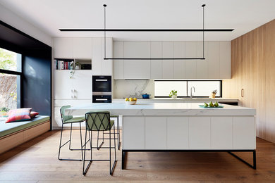 Design ideas for a contemporary galley kitchen in Melbourne with a submerged sink, white cabinets, white splashback, medium hardwood flooring, an island, brown floors, white worktops and flat-panel cabinets.