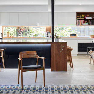 This is an example of a contemporary open plan kitchen in Brisbane with an undermount sink, flat-panel cabinets, white cabinets, wood benchtops, window splashback, black appliances, with island, beige floor and brown benchtop.