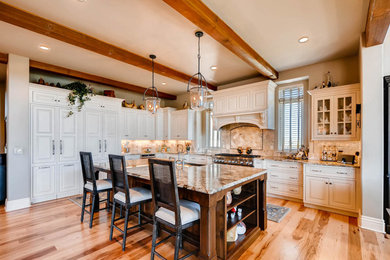 Large elegant l-shaped light wood floor and multicolored floor eat-in kitchen photo in Denver with a farmhouse sink, beaded inset cabinets, medium tone wood cabinets, granite countertops, beige backsplash, stone tile backsplash, stainless steel appliances and an island