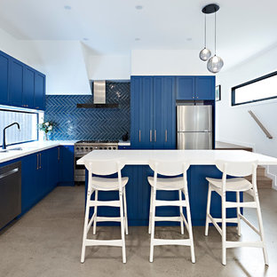 Mid-sized transitional l-shaped kitchen in Melbourne with a double-bowl sink, shaker cabinets, blue cabinets, blue splashback, stainless steel appliances, with island, white benchtop, ceramic splashback, concrete floors, grey floor and quartz benchtops.
