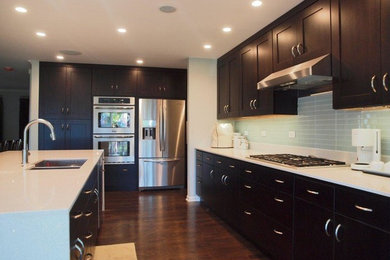 Eat-in kitchen - large contemporary l-shaped dark wood floor and brown floor eat-in kitchen idea in Chicago with an undermount sink, glass tile backsplash, stainless steel appliances, shaker cabinets, dark wood cabinets, solid surface countertops, blue backsplash and an island